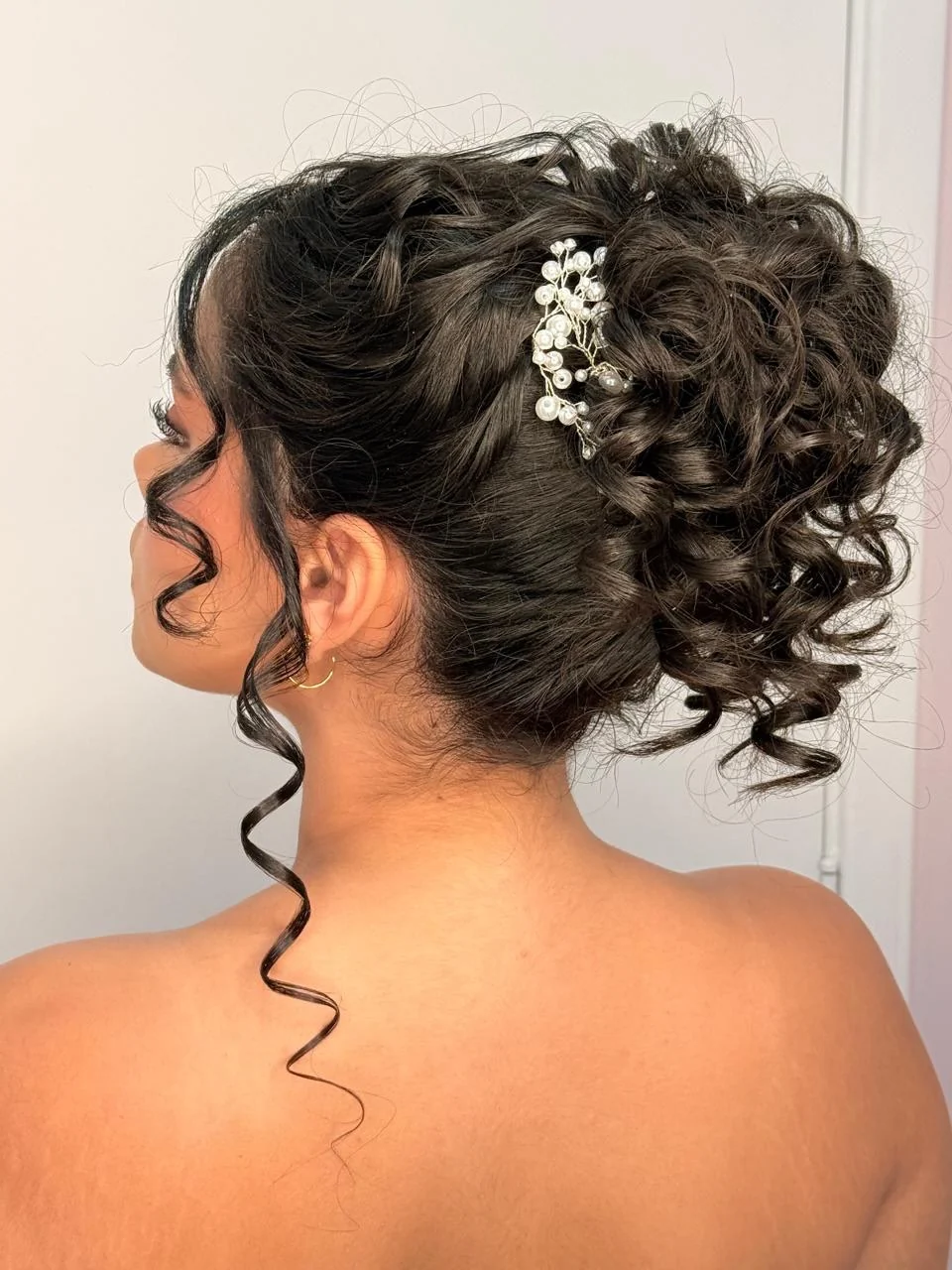 Penteado preso de cachos escuros com um pente de pérolas, visto por trás
